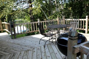 A wooden deck with a grill, metal chairs, and a table.