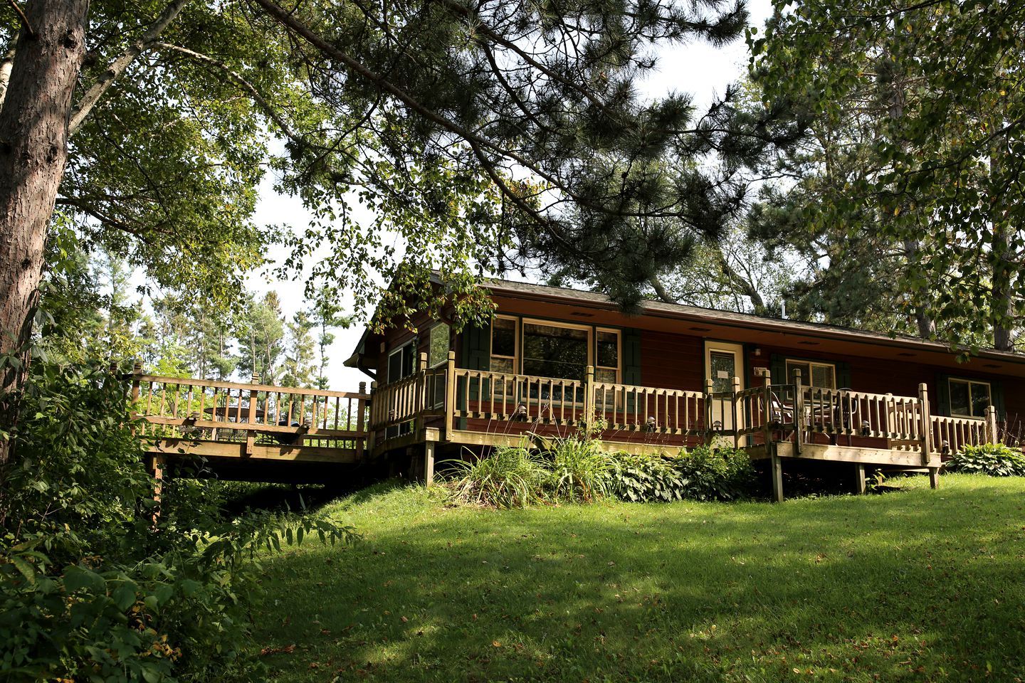 Une cabane en bois dotée d’une terrasse, entourée d’arbres et d’herbe.
