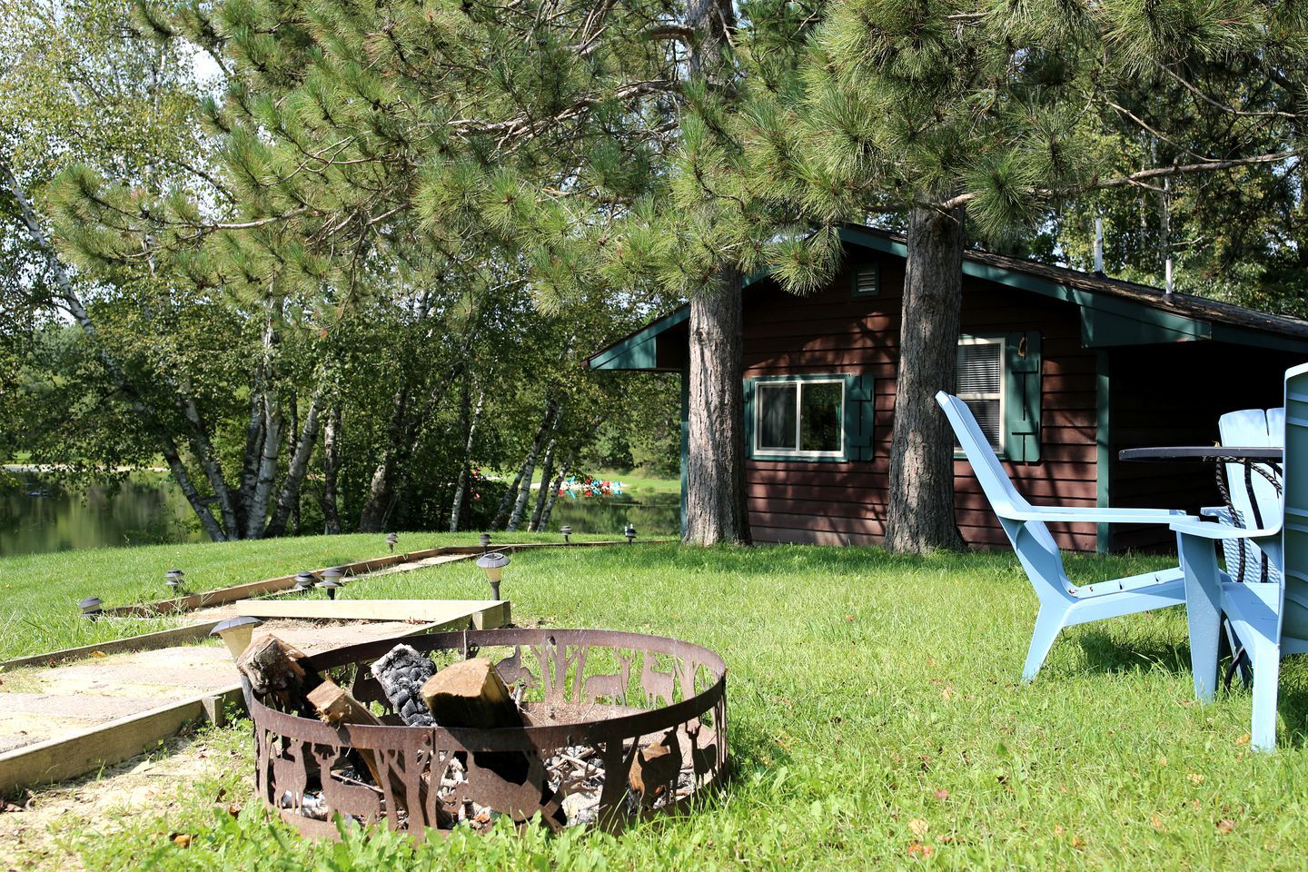 A rustic cabin with a fire pit, outdoor seating, and a pond in the background.