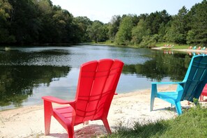 Two Adirondack chairs by a lake with a forest in the background. - Rustic Family Cabin Rental with a Fire Pit near Wisconsin Dells (Tomah)