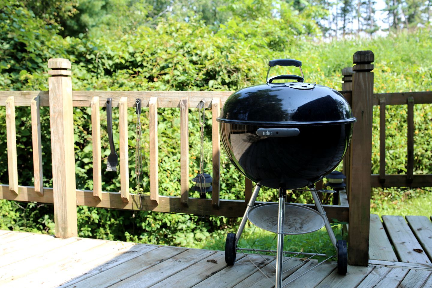 A Weber grill on a wooden deck with a wooden fence in the background.