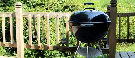A Weber grill on a wooden deck with a wooden fence in the background.