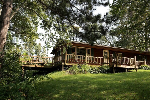 A wooden cabin with a deck, surrounded by trees and grass. - Rustic Family Cabin Rental with a Fire Pit near Wisconsin Dells (Tomah)
