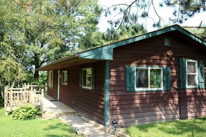 A wooden cabin with a porch, a fenced deck, and a small garden area. - Rustic Family Cabin Rental with a Fire Pit near Wisconsin Dells (Tomah)