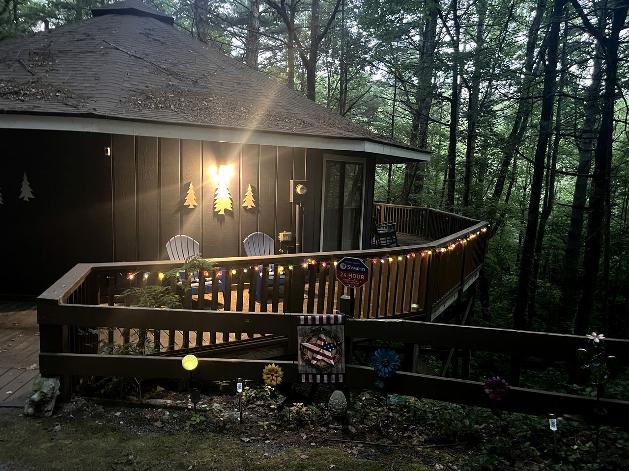 A wooden cabin with a deck, surrounded by trees.