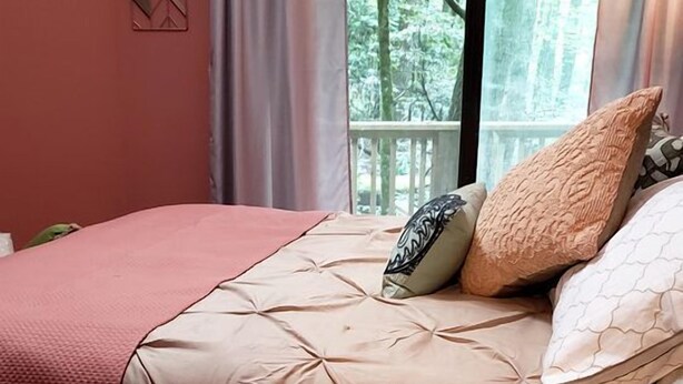 Ein Bett mit einer beigen Steude, zwei Kissen und einem Fenster mit Vorhängen.