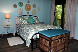 A bedroom with a bed, bedside table, lamp, decorative wall hangings, and a view through a window. - Rustic Tree Top Cabin in Sky Valley, Georgia (Sky Valley)