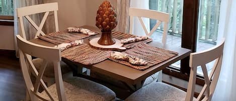 A dining area with a chandelier, white chairs, a wooden table, and a pinecone centerpiece.