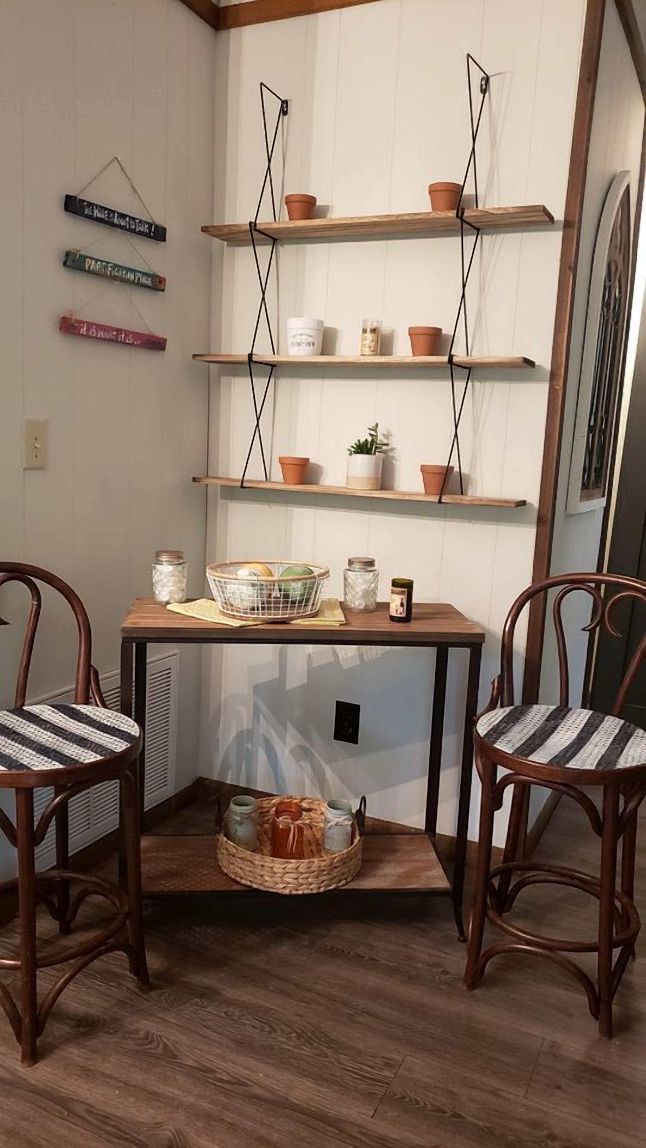 Ein Eckzimmer mit zwei Holzstühlen, einem Tisch mit einem Korb, Regalen mit Topfpflanzen und an der Wand befestigten Schildern.