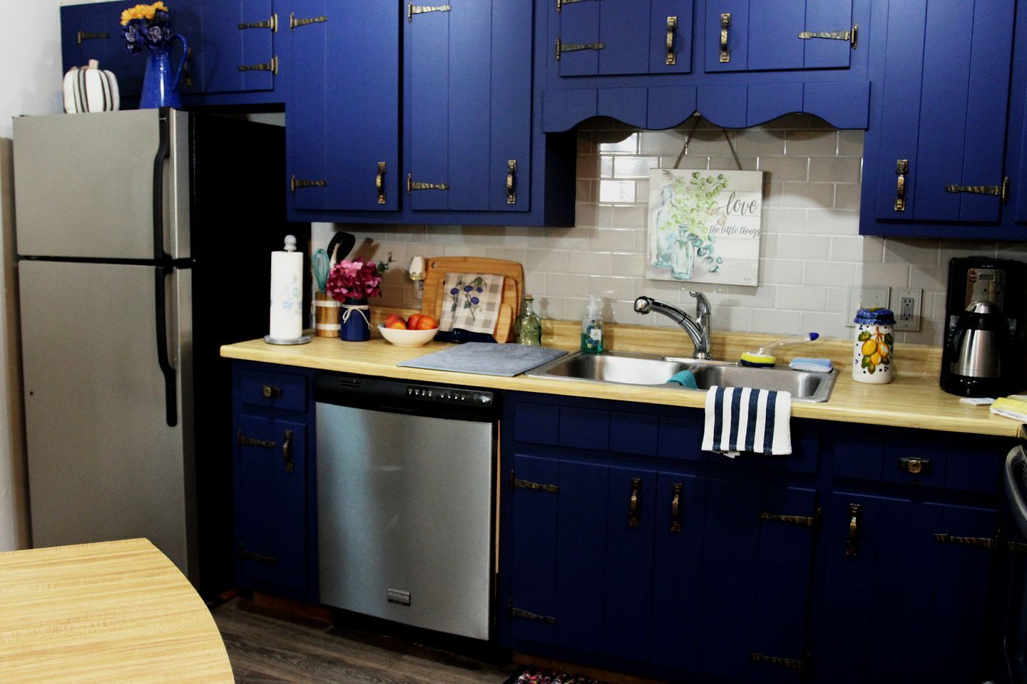 A kitchen with blue cabinets, a stainless steel dishwasher, a sink, and a coffee maker.