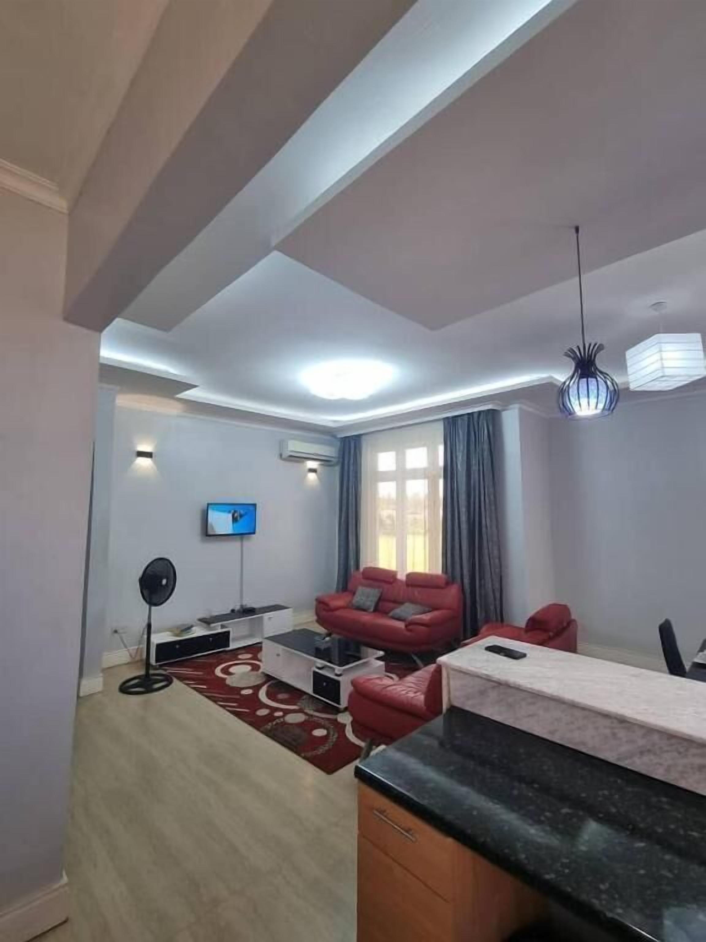 Una sala de estar moderna con una televisión de pantalla plana, un sofá rojo, una mesa de centro y un comedor con una mesa y sillas.