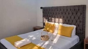A bedroom with a bed, a ceiling fan, an air conditioning unit, and a nightstand. - Legacy Homes 1B Apartment (Dar es Salaam)