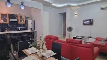 Una sala de estar moderna con comedor, sofás rojos, televisor y cocina con encimeras de mármol.