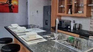 A modern kitchen with a granite countertop, bar stools, pendant lighting, and wooden cabinets. - Legacy Homes 1B Apartment (Dar es Salaam)