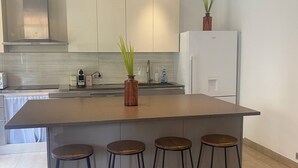 Una cucina moderna con isola centrale, sgabelli da bar, frigorifero e una pianta in vaso.
