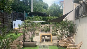 Un patio con erba sintetica, un tavolo di legno, sedie in vimini e piante in vaso.