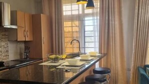 Una cocina con una isla central, taburetes de bar, luces colgantes y un ventanal con cortinas.