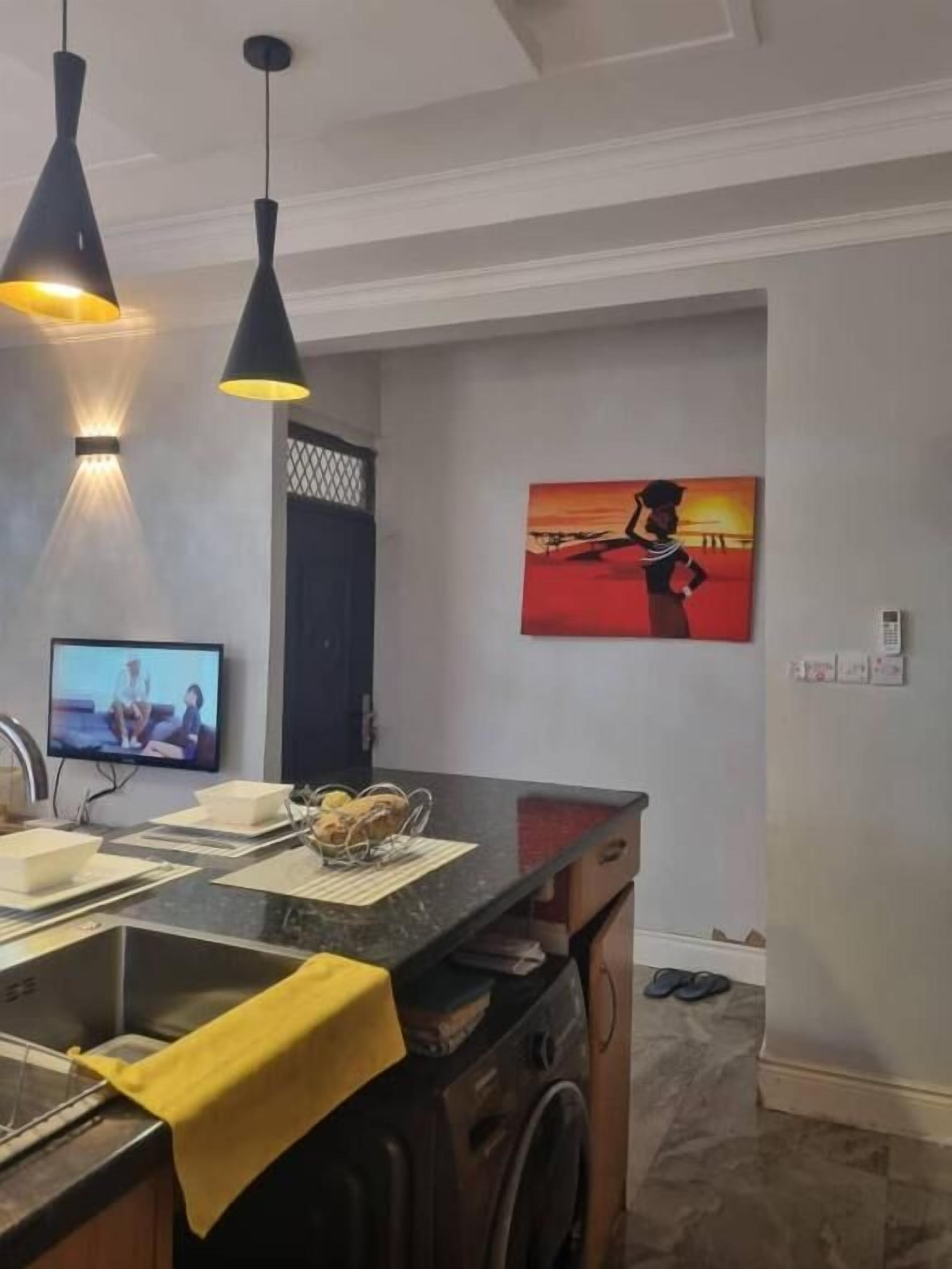Une cuisine moderne équipée d’un four encastré, d’un évier et d’un plan de travail. Un téléviseur est fixé au mur et un tableau est accroché au-dessus du plan de travail.