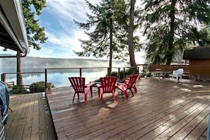 Eine Holzterrasse mit roten Stühlen, einem Tisch und Blick auf einen See.