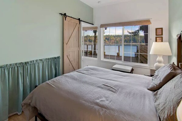 A bedroom with a bed, a window with a view of a lake, a wooden door, and a lamp.
