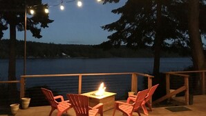 Une terrasse dotée d’un foyer, de chaises et de guirlandes lumineuses, offrant une vue sur une étendue d’eau.