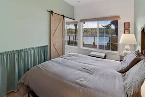 Ein Schlafzimmer mit Bett, einem Fenster mit Seeblick, einer Holztür und einer Lampe.