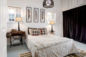 Un dormitorio con cama, dos mesitas de noche, lámpara, escritorio, silla, ventana y tres adornos de plumas en la pared.
