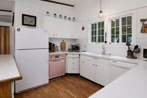 A kitchen with white cabinets, a pink stove, a white refrigerator, and a window with a view of greenery.