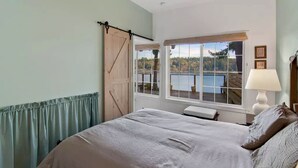 Una camera da letto con un letto, una finestra vista lago, una porta in legno e una lampada.