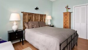 Une chambre à coucher comprenant un lit, deux tables de chevet avec des lampes, une tête de lit en bois, une commode et un placard.