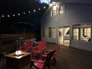 A deck with outdoor furniture and a fire pit, a house with large windows, and string lights.