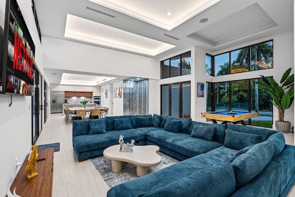 A modern living room with a large sectional sofa, a dining area, and a pool table.