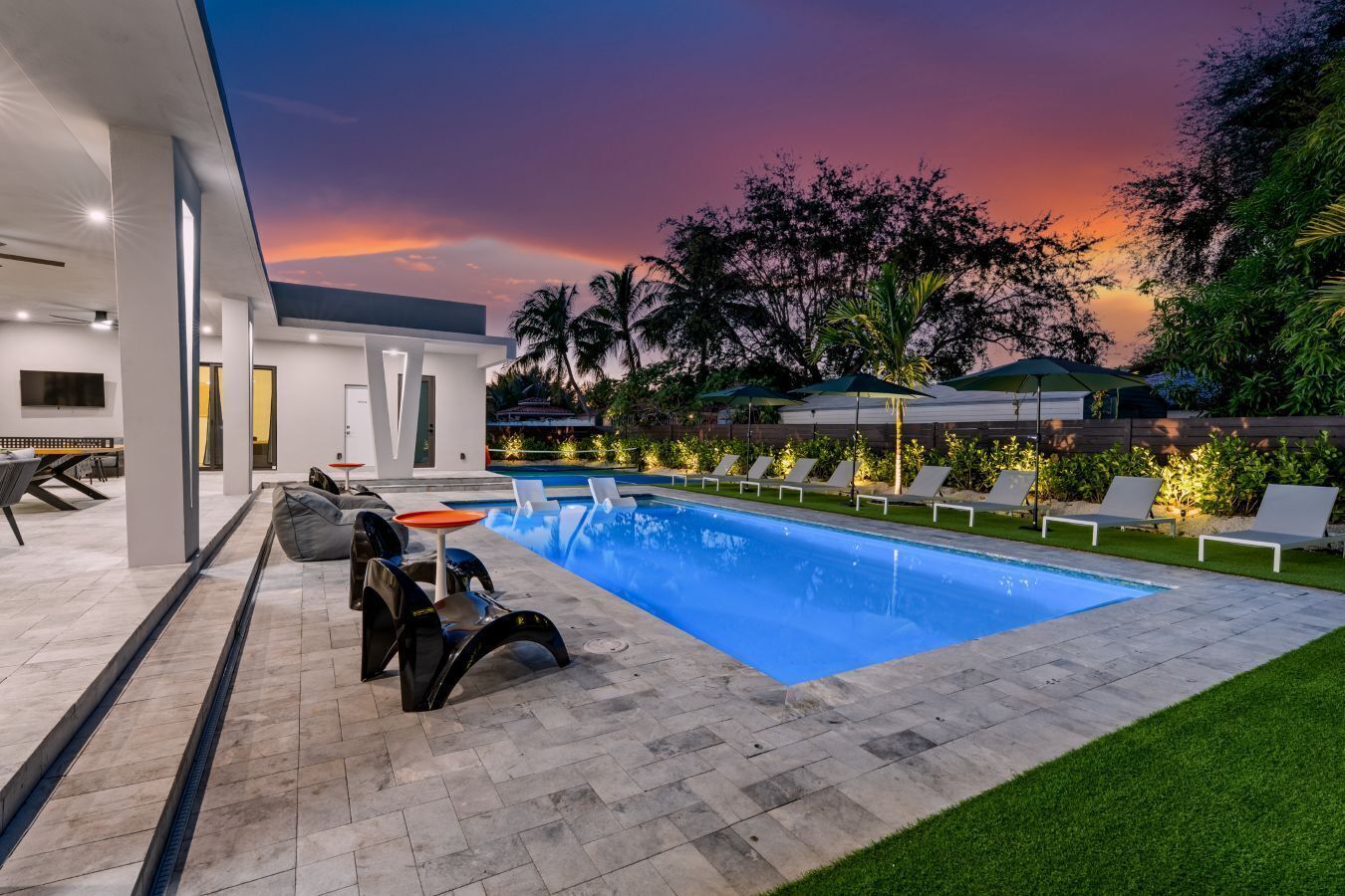 Un área de piscina moderna al aire libre con sillones de descanso, un espacio para sentarse y vistas al atardecer.