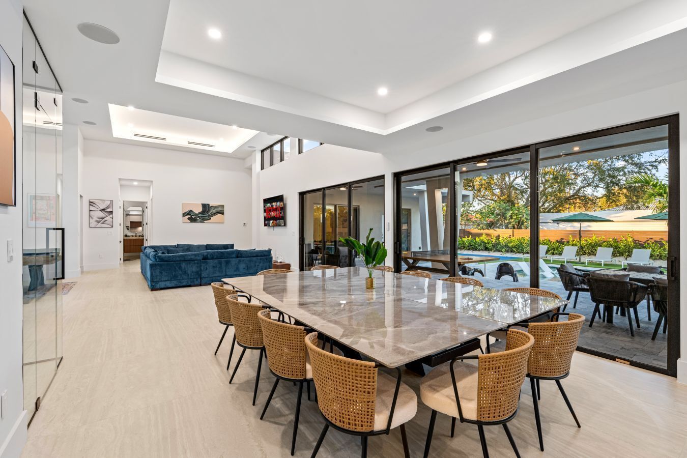 A modern interior with a dining area, a blue sofa, and a view of an outdoor pool area.