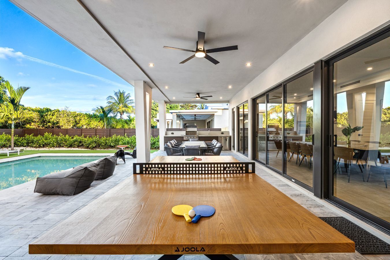 An outdoor dining area with a ping pong table, a pool, and a patio with a view of the backyard.