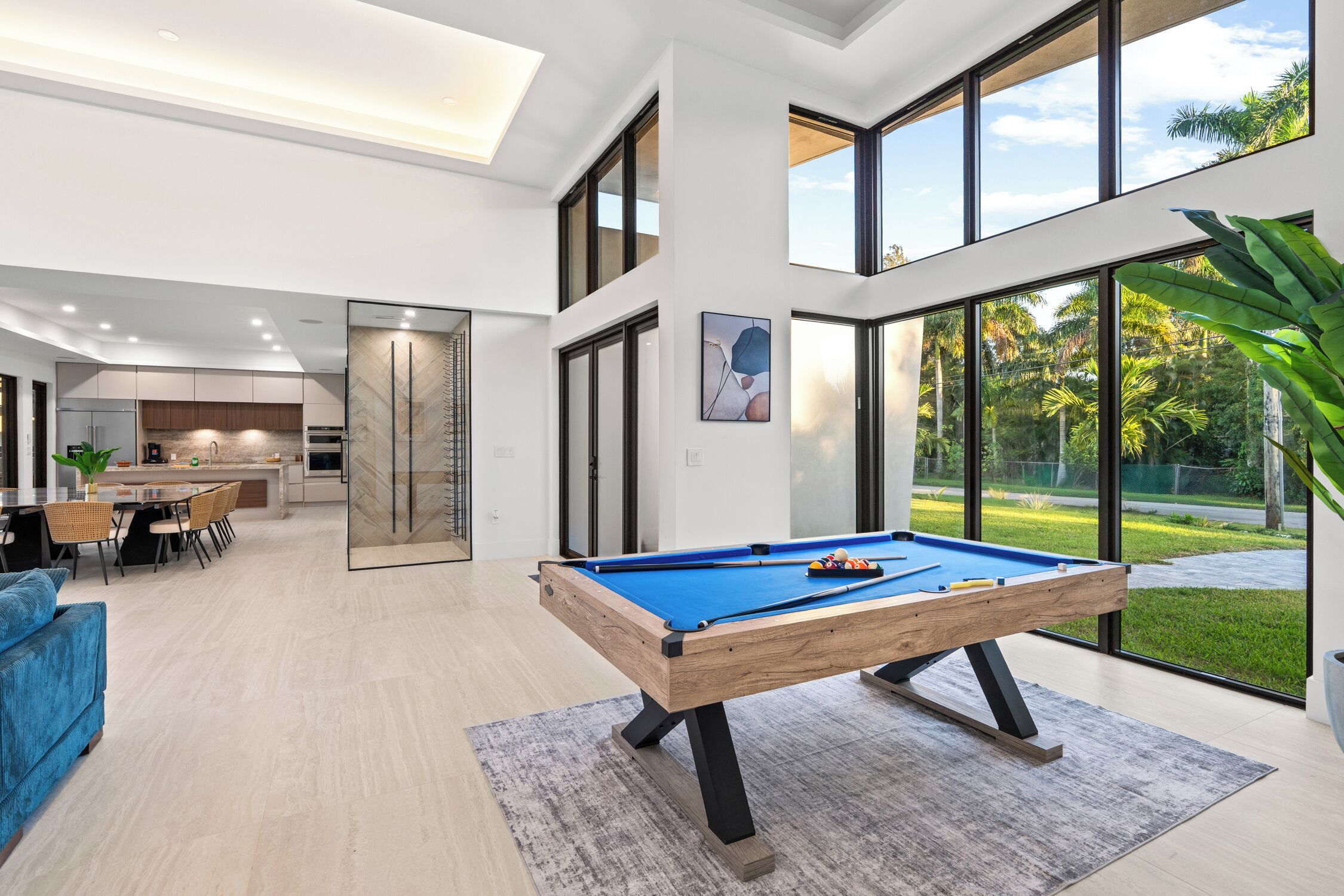 A modern living room with a pool table, a dining area, and a kitchen.