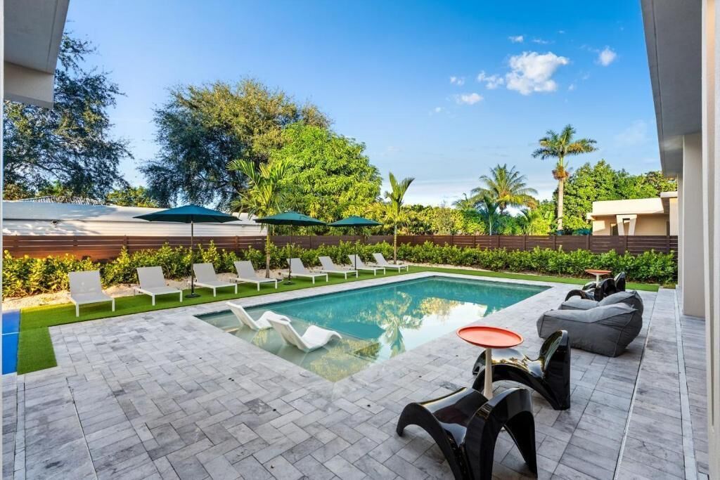 A swimming pool with lounge chairs and a table, surrounded by greenery and trees.