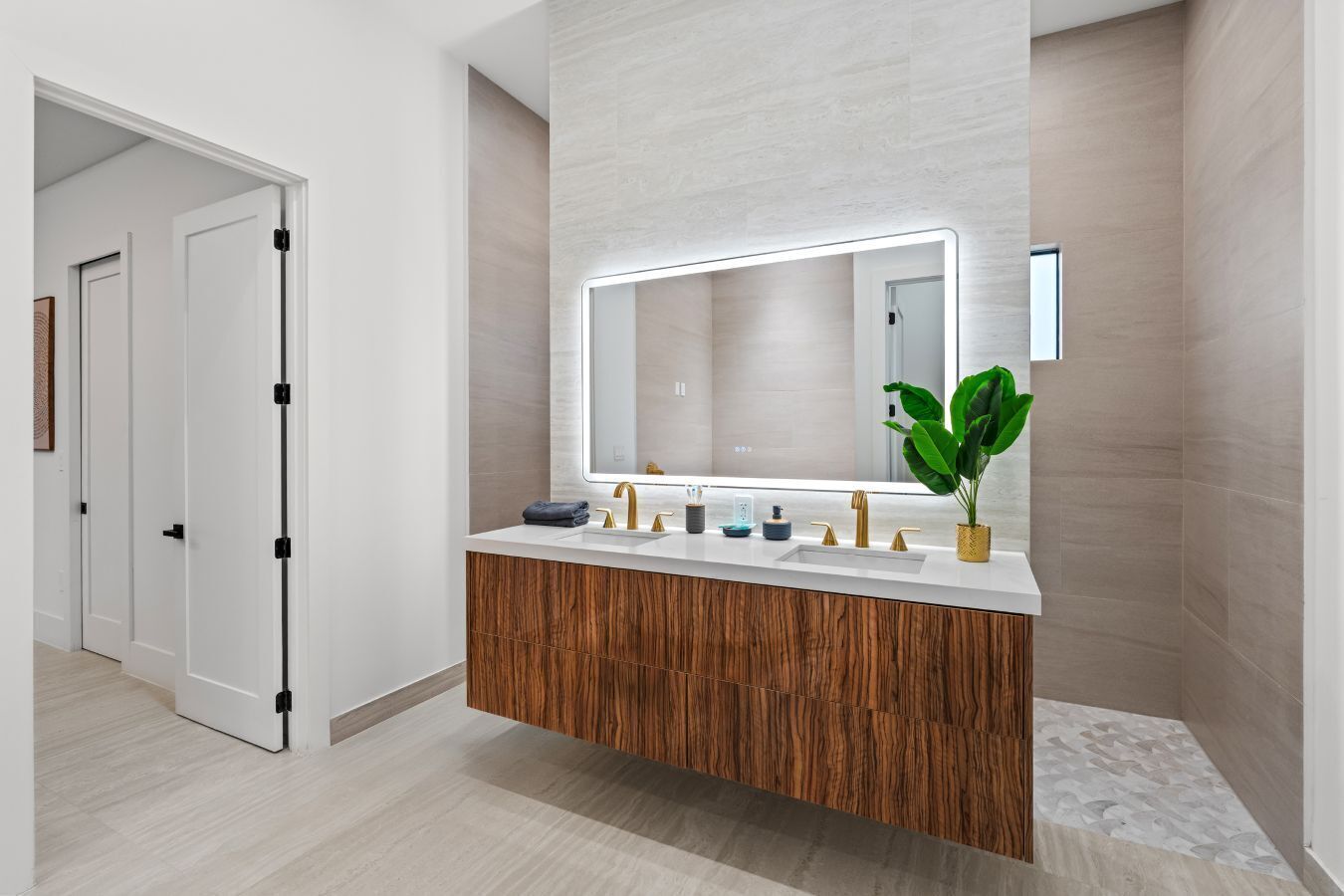 A modern bathroom with a wooden vanity, a large mirror, and a potted plant.