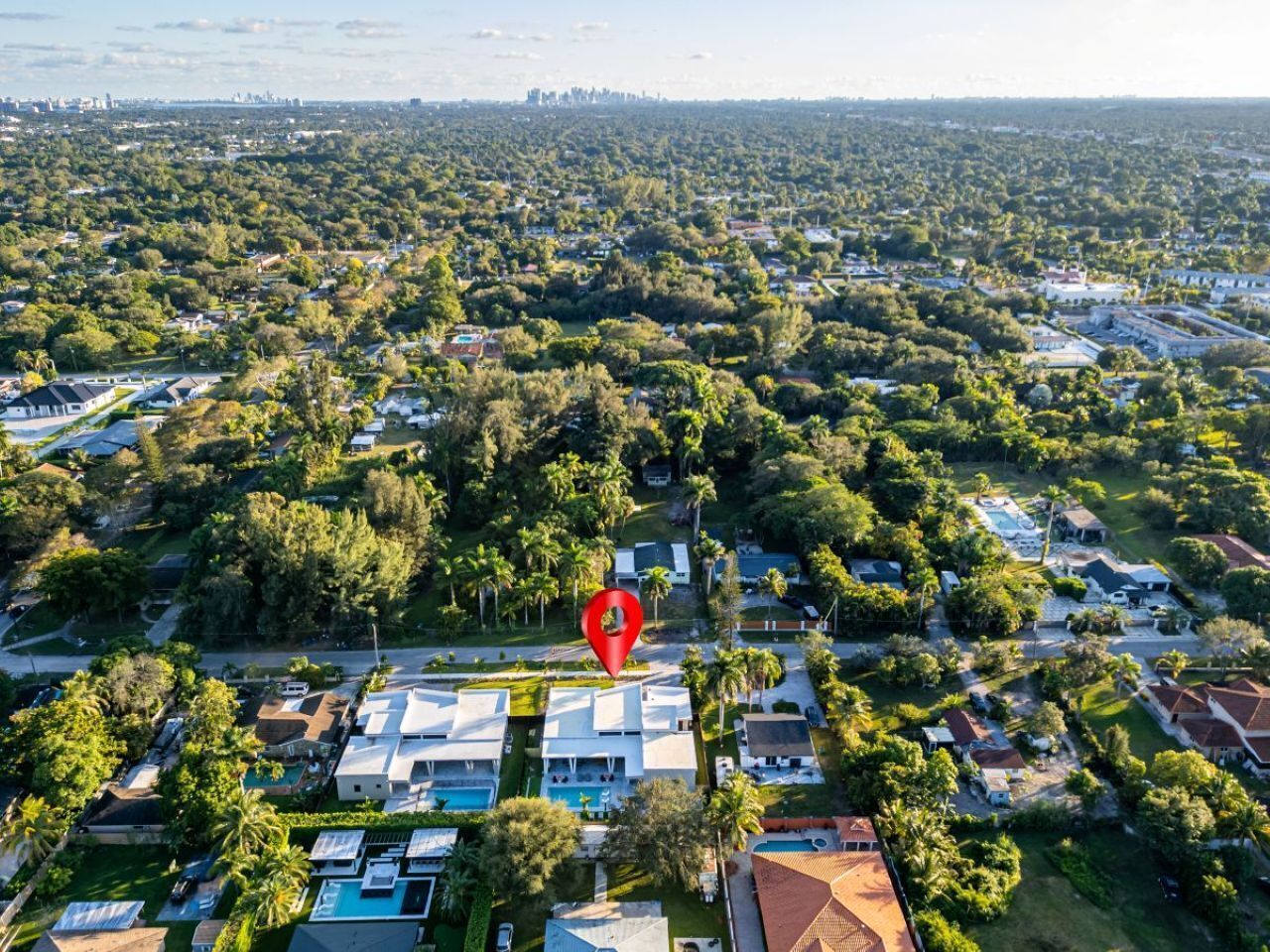 An aerial view of a residential area with houses, greenery, and a red location marker.