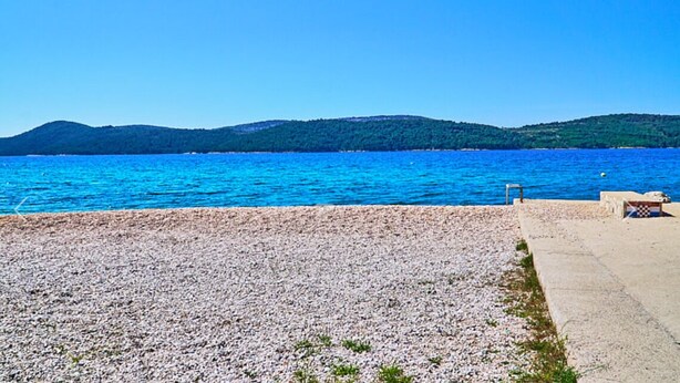 A pebbled beach with a clear view of the sea and distant hills.