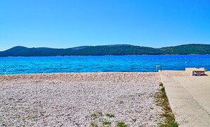 A pebbled beach with a clear view of the sea and distant hills. - 2-bedroom apartment in beautiful Šibenik with AC and charm (Šibenik)