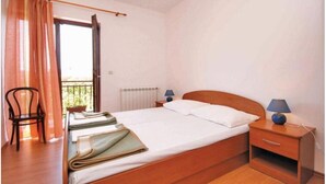A single bed with a wooden headboard, a nightstand with a lamp, a chair, and a window with curtains.