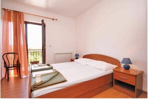 Un lit simple avec une tête de lit en bois, une table de chevet avec une lampe, une chaise et une fenêtre avec des rideaux.