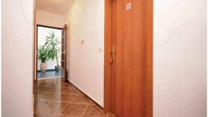 A hallway with a wooden door, a tiled floor, and a potted plant.