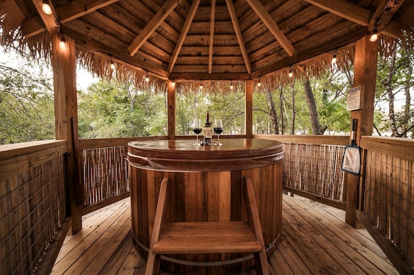 A wooden gazebo with a round table and chairs, surrounded by a wooden deck and bamboo fence, overlooking a forested area. - Luxury Glamping Yurt with Hot-Tub on the Medina River Bandera, Texas (Bandera)