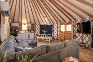 Un espacio interior acogedor con un sofá, una mesa de comedor, una zona de cocina y un televisor montado en la pared.