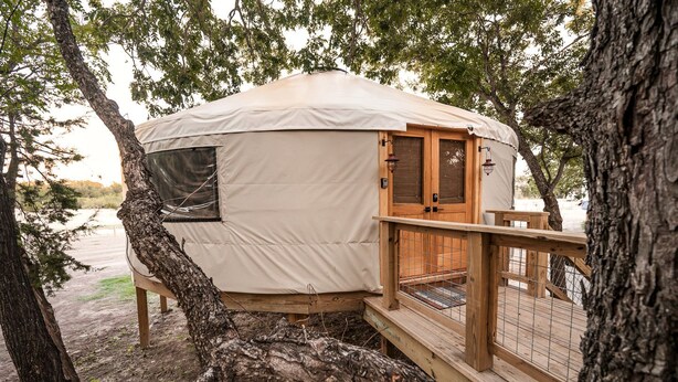 Une yourte dotée d’une terrasse en bois, d’une porte et d’une fenêtre.