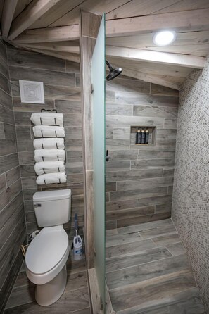 Un baño con techo de madera, inodoro, toallero y zona de ducha.