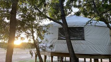 A tent-like structure with a window, supported by wooden posts, surrounded by trees.