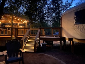 Un'area esterna riparata con una scala in legno che conduce a un patio, una struttura simile a una tenda con luci a stringa e una sedia.
